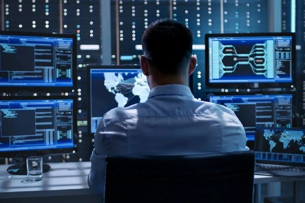 A man sitting in front of multiple computer screens.